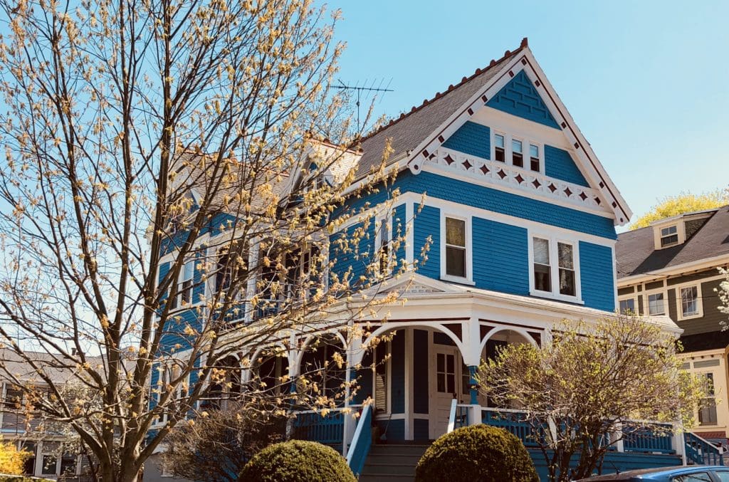 A 3 story blue home in Boston with a wrap around front porch