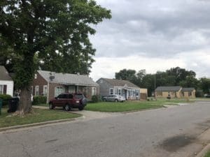 Nestled in a quaint Oklahoma City neighborhood, this residential street features small houses, a parked red SUV, and lush grassy lawns under overcast skies—a charming slice of real estate offering both tranquility and community.