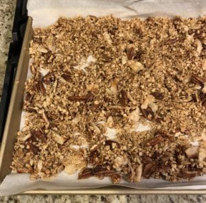 A baking sheet of homemade granola with oats, pecans, and coconut on parchment paper showcases a delightful granola recipe.