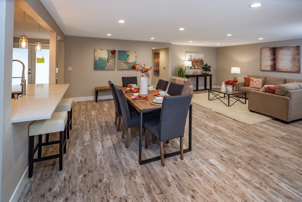 Modern open-plan dining and living area designed with house flipping in mind, featuring a wooden floor, a table set for six, beige sofas, and contemporary decor.