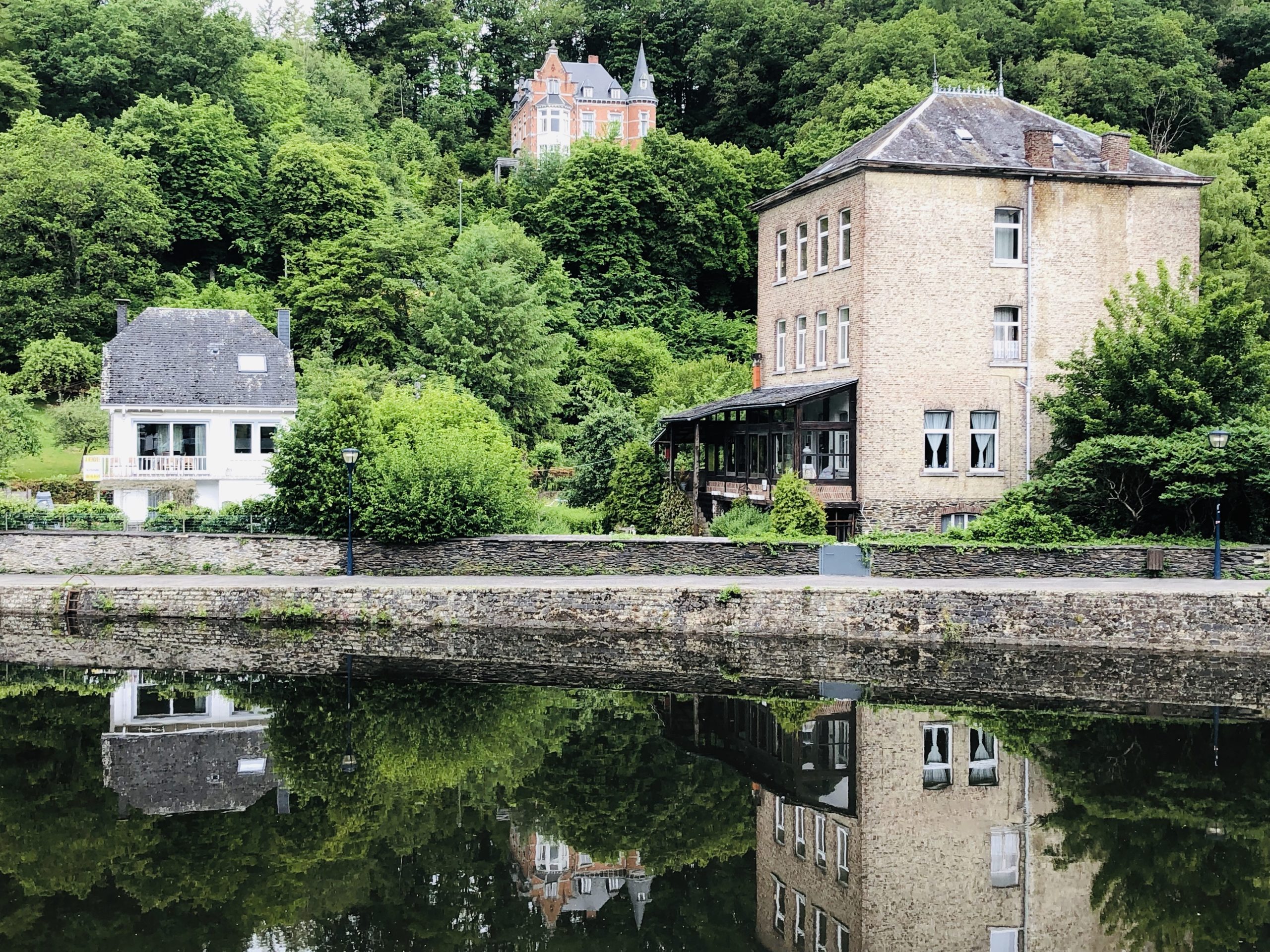 Two houses are reflected in a calm river, surrounded by lush greenery and a small hill with more trees in the background—a serene setting, as reassuring as title insurance for homeowners.