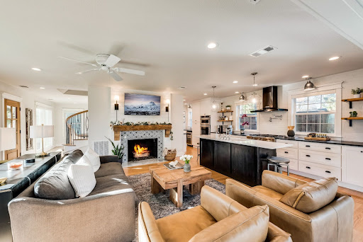 Open-concept living room and kitchen with a fireplace, sofa, armchairs, and a central coffee table. Recent purchases enhance the space, like the light fixtures hanging over the kitchen island. The room is bright with neutral tones.