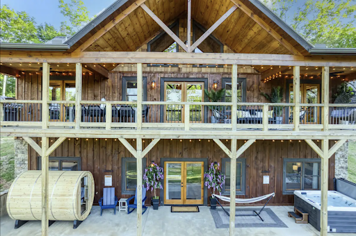 Best short-term rental market Blue Ridge, GA A rustic two-story log cabin, perfect for short-term rental markets, features a balcony, outdoor seating, a wooden sauna barrel, a hammock, and a hot tub on the ground level.
